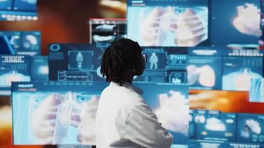 Bilimadamı video taramalarını izliyor. 360 derece dönüşe ayarlı. Laboratuvar önlüğü giyen kadın dijital sağlık göstergesi önünde insan anatomisini ve kamerayı analiz ediyor.