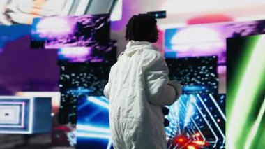 Astronot kıyafeti giyen gülümseyen kadın dijital arkaplanda soyut renkli görsellerin önünde dans ediyor. Mutlu uzay kaşifi dans hareketlerini parlak neon girdabına karşı izole eder, kamera B