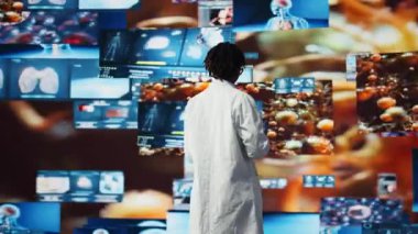 Doktor not defterindeki genomlara bakıyor, enfeksiyon modellerini karşılaştırıyor. Biyomedikal uzman laboratuvar önlüğü giyiyor patojenler üzerinde çalışıyor antiviral stratejiler tasarlamak için dizüstü bilgisayar kullanıyor, kamera A