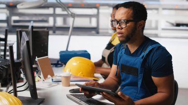 PC ve tabletle parametreleri karşılaştırarak fotovoltaik fabrikasındaki arızalı sistemleri araştıran bir mühendis. Siyahi adam güneş panellerini inceliyor üretim tesisi, yüksek teknoloji. Kamera A.