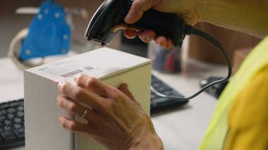 Asyalı bir çalışan nakliye etiketleri takıyor ve takip bilgilerini tarıyor, teslimat sırasında kargo bilgilerini kaydediyor. Depodaki görevleri Hi vis Yeleği ile etiketliyor. Kamera B.