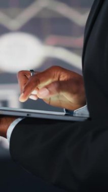 Karar vermeden önce KPI şirketinin dijital video verilerini karşılaştırmak için tablet kullanan bir iş kadınının dikey görüntüsü. Girişimci aygıt uygulaması kullanarak anahtar performans göstergelerini analiz ediyor