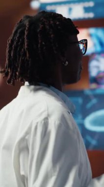 Dikey video görüntüsü, video kasetteki tıbbi taramaları inceleyen neşeli bilim adamı. Laboratuvar önlüğü giyen mutlu araştırmacı dijital sağlık panelinin önünde duruyor, insan anatomisini analiz ediyor.