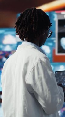 Dikey video Epidemiyoloji uzmanı bilgisayar ekranında viral mutasyon modellerini inceliyor. Aşı gelişimini desteklemek için dizüstü bilgisayardaki 3D virüs yapısını inceleyen bilim adamı, çevresi tıbbi panellerle çevrili.