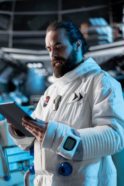 Astronot araştırmacısı uzay gemisi sensörlerini tablet kullanarak kalibre ediyor, araştırma yapıyor. Uzay gemisinde kozmonot kıyafeti giyen bilim adamı uçuş sırasında güvenlik kontrolü yapıyor.