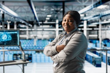 Gülümseyen veri merkezi teknisyeninin portresi. Yapay zeka otomasyon senaryolarının kodlarını incelemekle görevli. Sunucu merkezindeki mutlu Afrikalı Amerikalı kadın yapay zeka yönetiyor.