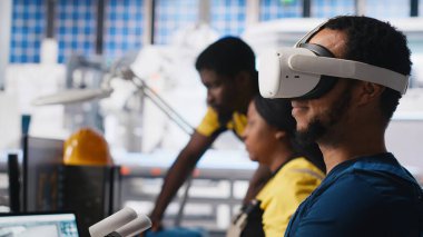 Fotovoltaik fabrikası mühendisi VR kulaklıklı PC CAD yazılımı tasarlıyor, güneş panelleri imalat fabrikasında çalışıyor. Siyah uzman sanal gerçeklikteki montaj hatlarını inceliyor. Kamera A.