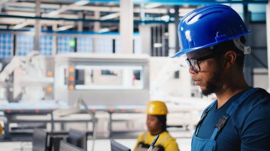 Siyah fotovoltaik fabrikası teknisyeni evrakları inceliyor, üretim verilerini analiz ediyor. Güneş panelleri, sorun çıkarmak için dosya okuyan fabrika işçisi üretiyor. Kamera B.