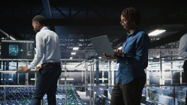 Veri merkezi endüstriyel platformundaki sistem yöneticileri dizüstü bilgisayardaki performans çıktılarını analiz ediyorlar. Sunucu merkezi iş arkadaşları dizüstü bilgisayar kullanarak sunucu sondaj ayarlarını inceliyor,