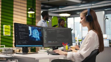 Ofisteki genç bayan programcı yapay zeka ölçümlerini inceliyor, müzik dinliyor, performans göstergelerini izliyor. Küçük Dev kulaklık takıyor sinirsel ağları ayarlıyor PC 'deki araçları kullanıyor, kamera A