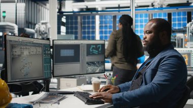 Afrika kökenli Amerikalı usta mühendis bir güneş teknolojisi fabrikasında yeşil enerji hedeflerine ulaşmak için fabrika faaliyetlerini inceliyor. Uzman, üretim verimliliği için tablet kullanır. Kamera A.