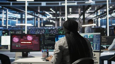 Sunucu çiftliği bilişim uzmanı bilgisayar monitöründe görülen güvenlik ihlali uyarısına yanıt veriyor, donanımı güvence altına almak için çalışıyor. Veri Merkezi çalışanı siber saldırı sırasında ekipmanları korumaya çalışıyor, kamera A
