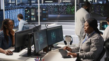 Veri merkezi geliştirici kodlaması PC 'de, yapay zeka süper bilgisayarları için yazılım güncellemeleri yapıyor, saate bakıyor. Sunucu çiftliği bilişim uzmanı yapay zeka ve kamera A kullanarak altyapıyı optimize ediyor.