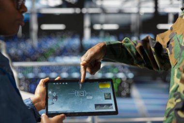 Askeri teknisyen sunucu merkezindeki tablet ekranda taktik gösterge panelini inceliyor. Endüstriyel platformda duruyor. Stratejik iletişim ve altyapı yazılım sistemleri kullanan ordu uzmanı.