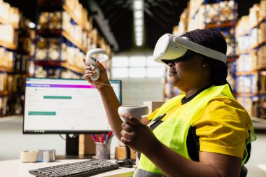 Siyah kadın çalışan, dijital paket izleme yazılımı, yapay zeka envanter yönetimi ve lojistik merkezdeki sipariş işleme paketlerinin durumunu izlemek için VR gözlüğü kullanıyor. Sanal gerçeklik.