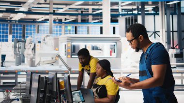 Güneş paneli fabrika teftişinde müfettiş üretim ekipmanları ve üretim süreci, belge dosyalarını kontrol ediyor. Siyahi adam tesiste çevre dostu fotovoltaikleri sağlıyor. Kamera B.