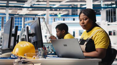 Afrika kökenli Amerikalı kadın çalışanlar, yenilenebilir enerji üretim endüstrisinde çalışarak çoklu güneş paneli tasarımlarını CAD yazılımı üzerinde test ediyorlar. Üretimi optimize eden kadın mühendis. Kamera B.