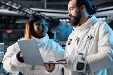 Astronotlar, gelecekten gelen uzay gemisindeki meslektaşları dizüstü bilgisayardaki görev verilerini izliyorlar. Özel teçhizat giyen uzay adamları defter kullanarak uzay yolculuğu operasyonlarına hazırlanın.