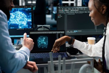 Veri merkezinde baş programcı ve kadın mühendis yapay zeka otomasyon senaryolarını güncelliyor. Sunucu odası bilişim uzmanı ve masasında yapay zeka algoritmaları programlayan Afrikalı Amerikalı kadın.