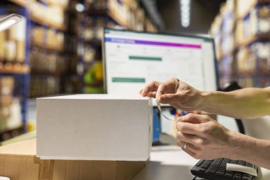 Paketleme istasyonundaki Asyalı bir lojistik işçisinin yapışkan hava yolu faturası uygulamasını etiketlerdeki sevkiyat detaylarıyla sipariş takibini yönetmesini. Büyük ölçekli e-ticaret ürünü dağıtımı.