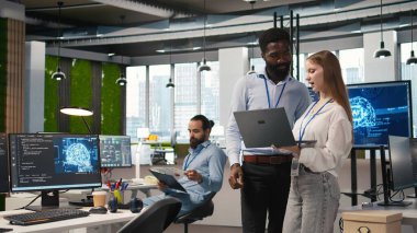 Küçük Dev ve meslektaşı yapay zeka sistem ölçümlerini gözden geçiriyorlar. Performans gösterge panellerini izliyorlar. Teknoloji şirketi programcısı ve genç bayan mühendis sinirsel ağları ayarlıyorlar, kamera A