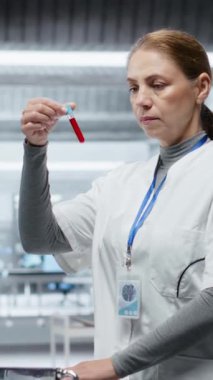 Dikey Video Bilimadamı modern laboratuvar ortamında test tüplerini kanla inceliyor, yeni bir ilaç test ediyor ve yan etkilerini kaydediyor. Güvenlik ve etkinliği sağlamak için dozaj tepkisi analiz ediliyor