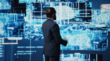 Şirket lideri, akıllı yenilikler ve gelecekteki teknoloji stratejileri için makine öğrenimi ve algoritma geliştirme yöntemlerini kullanarak ağ platformlarını sembolize eden dijital yapay zeka beyniyle etkileşim halindedir. Kamera B.