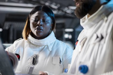 Uzay gemisindeki kadın astronot bilim adamı ve meslektaşı yörüngede bilimsel deneyler yapıyor. Kozmonot kıyafeti giyen kadın araştırmacı ve uzay gemisinde araştırma yapan iş arkadaşı.