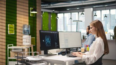 Küçük dev üretici yapay zeka makinesini test ediyor algoritmaları öğreniyor ve iş yerinde müzik dinliyor. Kulaklık takan genç bir kadın yapay zeka ile verimliliği artırıyor.