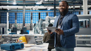 Bir güneş enerjisi üretim tesisinde çalışan Afrikalı Amerikalı teknisyen şirket denetimi ve ekipman üretimini yansıtmak için takım elbise giymiş operasyonları değerlendiriyor. Temiz enerji. Kamera A.