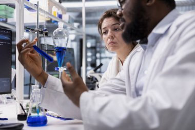 Laboratuar çalışanları test tüpündeki reaktörleri inceleyip klinik deneylerde çığır açan bulgular arıyorlar. Araştırma tesisi uzmanı birlikte çalışıyor, kimyasal şişeleri karşılaştırıyor, formülü test ediyor.