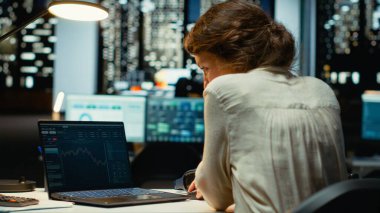 Ofisteki profesyonel işçi, ticareti optimize etmek ve gelir hedeflerine ulaşmak için veri analizi, tahmin ve finans stratejisi kullanarak dizüstü bilgisayardaki hisse eğilimleri ve şamdan çizelgelerini izliyor. Kamera B.