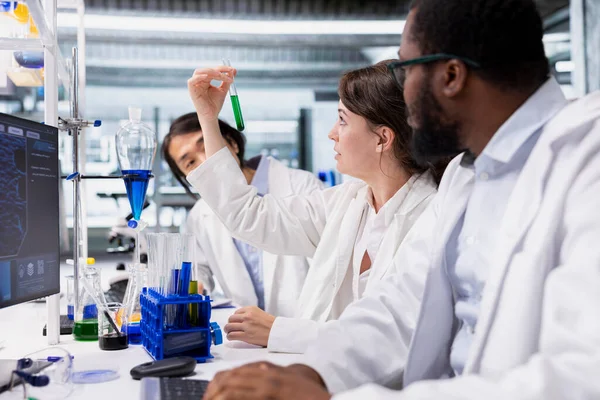 Laboratuvar teknisyenlerinden oluşan çok ırklı bir ekip saflık doğrulaması için kimyasal çözeltiyi şişelerde inceliyor. Araştırma tesisi çalışanları beyin fırtınası yapıyor, test tüplerini test prosedürleri için hazırlıyorlar.