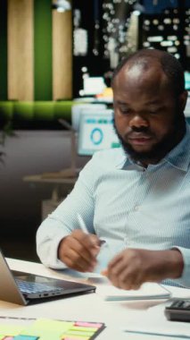 Bir sunum için el yazısı notları hazırlayan Dikey Video Siyah iş uzmanı, finans belgelerinden temel verileri ayıklıyor ve iş hedefleri ve görevleri için güncellemeleri içeren bir özet yapıyor