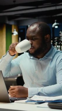 Bir kupadan kahve yudumlayan ve kapanış ofisini kuran dikey Afrikalı Amerikalı işçiler, geç saatlerin farkına varıyor ve ayrılma görevini tamamlıyor. Genç çalışanlar fazla mesaiden sonra evlerine dönüyorlar. Kamera.