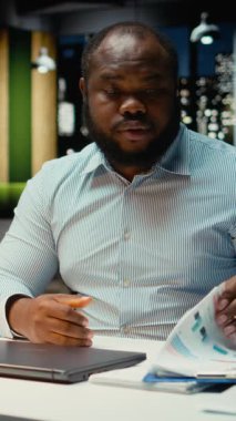 Dikey Video Siyah erkek çalışanı, çalışma saatleri dışında lambasını ve laptopunu kapatıyor, teslim tarihlerine yetişmek ve hedefe ulaşmak için gece geç saatlere kadar çalışıyor. Fazla mesai yapıyor ve strateji geliştiriyor.