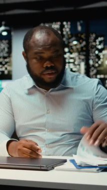 Dikey Video Siyah genç işadamı gece yarısı görevlerini tamamlıyor ve lambasını kapatıyor, karmaşık proje için fazla mesai yaptıktan sonra ofisinden aşırı yüklenmiş ve yorgun bir şekilde ayrılıyor. Kilitliyorum. Kamera A.