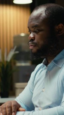 Dikey Videolu Sinirli Zenci Adam yoğun iş yükünden dolayı sinirleniyor, saatler sonra hayal kırıklığı ve rahatsızlık içinde çalışıyor. Endişeli huzursuz çalışan karanlık ofiste bunalıyor.