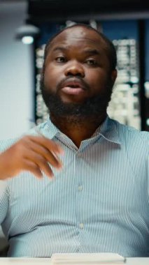 Dikey Video Siyah iş adamı karanlık ofisten çevrimiçi video görüşmesi yapıyor, web kamerasında göz teması kuruyor. Anlamlı konuşmalar için toplantıya katılmak, yatırımcılarla yakınlık kurmak