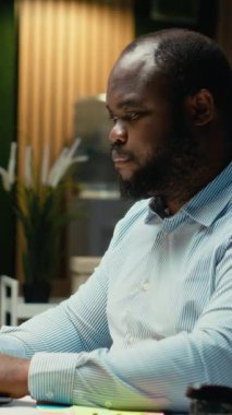 Dikey Video Siyah iş danışmanı not olarak dizüstü bilgisayara yapışkan bir not bırakıyor. Yapılacaklar listesinden bir görevi hatırlamaya çalışıyor. Geç saatlere kadar çalışıyor ve ertesi sabah için bir hatırlatma bırakıyor. Kamera B