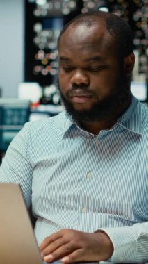 Dikey Video Afrikalı Amerikalı bir hatırlatma olarak sarı bir not etiketi yazıyor, mesai bitiminden sonra ofiste bir işi bitirmeye çalışıyor. Erkek çalışanın not olarak yapışkan bir not etiketi koyması, kırtasiye