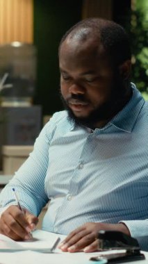 Dikey Afrikalı Afrikalı Amerikalı bir insan bir hata yaptıktan sonra kağıt sayfasını yırtıyor, el yazısı ve mesai sonrası not tutuyor. Sinirli bir çalışan yeni bir çarşafın taslağını yeniden hazırlıyor. Kamera B.