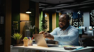 Afro-amerikan ofis çalışanı laptopuna yapışkan bir not bırakıyor, yapılacaklar listesinden bir görevi hatırlamaya çalışıyor. Gece çalışıyor ve ertesi sabah için not bırakıyordu..