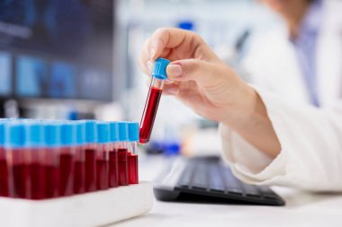 Araştırma tesisindeki çalışma istasyonunda kırmızı gösterge çözeltisiyle dolu laboratuvar camları kullanarak kimya mühendisliğine yaklaş. Laboratuvar uzmanı deney için kullanılan kimyasal sıvıyla şişe seçiyor.