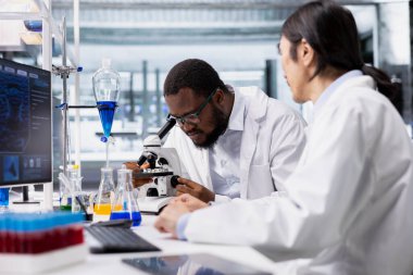 Araştırma tesisi çalışanı, klinik bank çalışma istasyonunda biyolojik materyalleri büyütme aracı ile gözlemler. Biyokimyacı laboratuardaki hücresel yapıları incelemek için mikroskop kullanır, deneyler yapar.