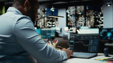 Afrika kökenli Amerikalı danışman hisse senedi ve ön ödeme verilerini inceliyor, iş gelişimini yönlendiren raporlar ve tahminler hazırlıyor. Geceleri modern bir yatırım stratejisi oluşturmak..