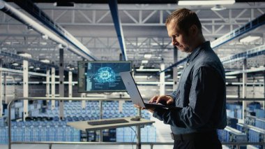 Teknisyen tesiste yürürken laptop kullanarak sunucu odası aktivitelerini izliyor. Veri Merkezi IT profesyonel incelemeleri sistemlerin doğru çalıştığından emin olmak için test sonuçları, kamera A