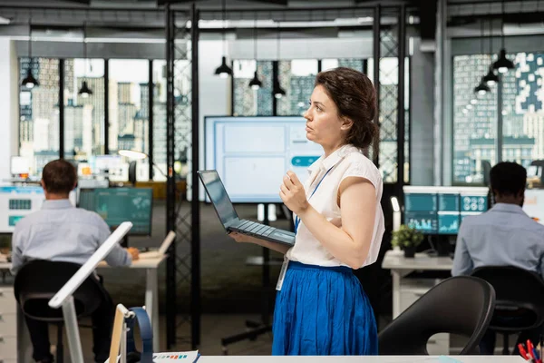 Dizüstü bilgisayarla çalışan profesyonel bayan yönetici, yaklaşan yönetim kurulu tartışmaları için strateji planlıyor. Düşünceli iş kadını ayakta duruyor ve çok uluslu şirket büyümesi için yenilikçi projeler düşünüyor