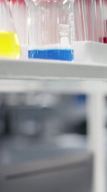 Laboratuar rafındaki bilimsel cam kaplamaların içindeki renkli kimyasal çözümlerin dikey videosu. Şişelerdeki reaktifler, yüksek teknoloji araştırma merkezinde deneysel analiz için kullanılmaya hazır.