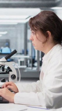 Dikey video Nanoteknoloji araştırmacısı zamanı kontrol ediyor, vardiyayı bitirmeyi bekliyor, hasta verilerini işliyor. Laboratuvar çalışanı genetik analiz yapmak için bilgisayar kullanıyor. Kol saatini kontrol ediyor. Kamera B.